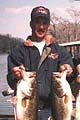 Two Men Proudly Display Large Bass Fish While Standing On A Boat