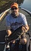 A Man Wearing A Hat And Sunglasses Proudly Holds A Large Bass Fish